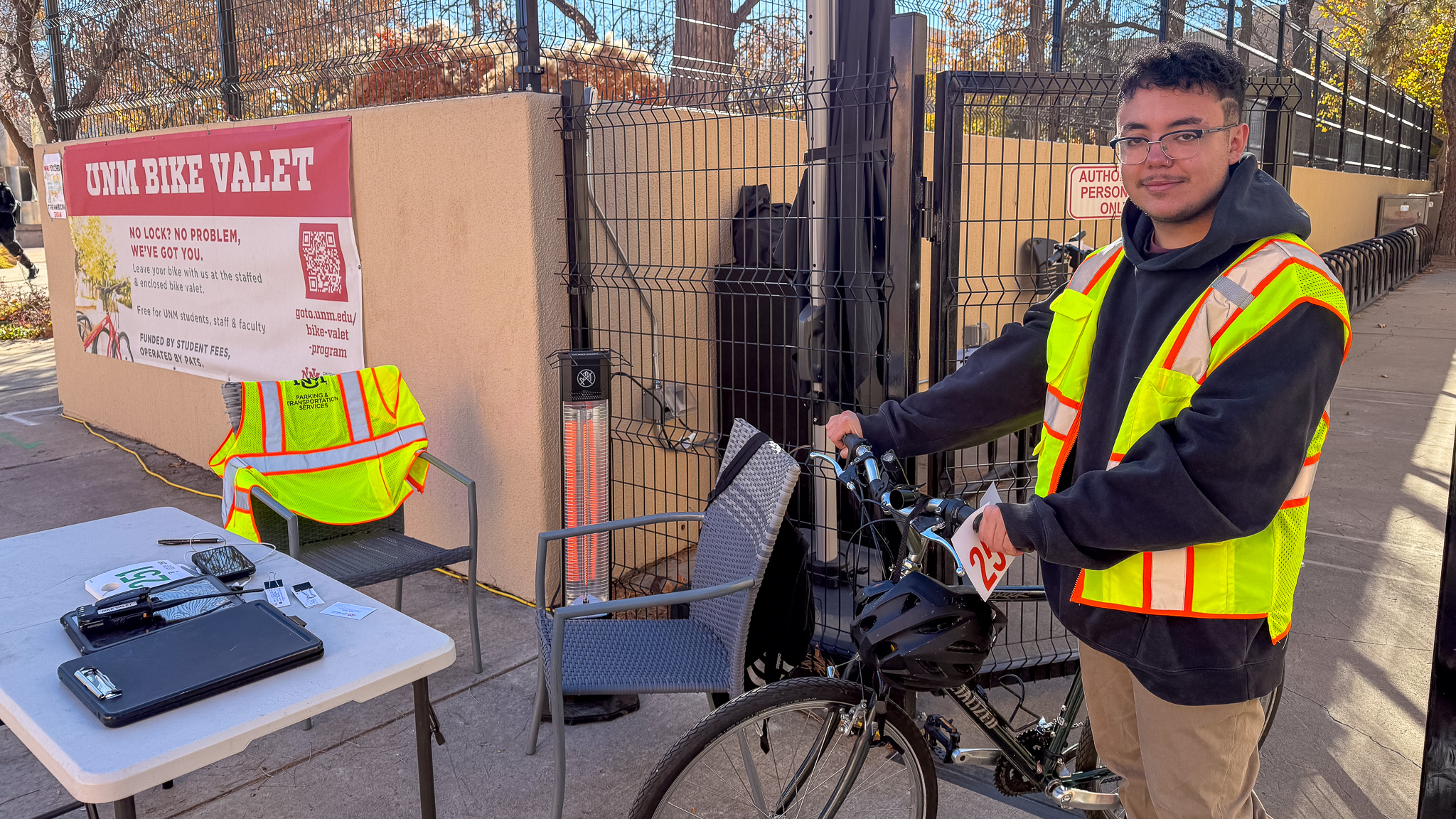A UNM student wearing a helmet and red UNM Lobos t-shirt stands next to her bike.