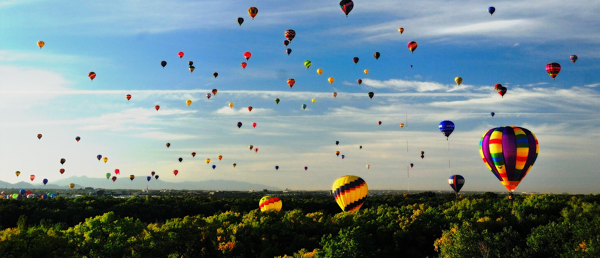 Hot air balloons rising over a tree line.