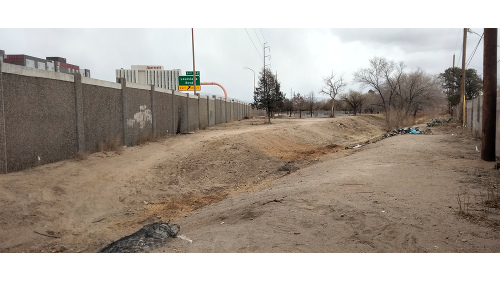 Image of the Tom Bolack Trail extension before January 2025. Image depicts dirt trail next to I-40 at Louisiana, littered with trash and debris.
