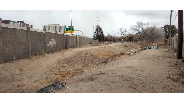 Image of the Tom Bolack Trail extension before January 2025. Image depicts dirt trail next to I-40 at Louisiana, littered with trash and debris.