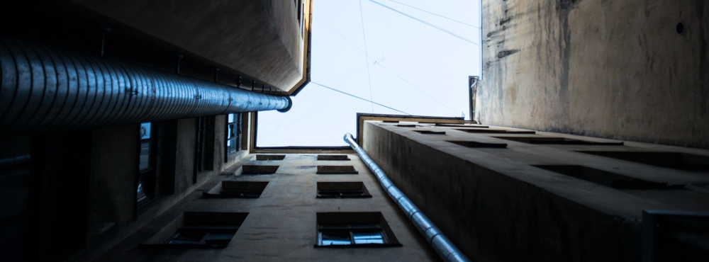 The view from the ground in an alley looking up the walls of buildings at the sky.