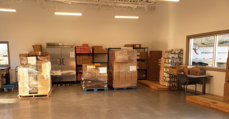 A jpg of the Alamosa Food Pantry, featuring boxes, cans, and other containers of donated food stacked against a wall.