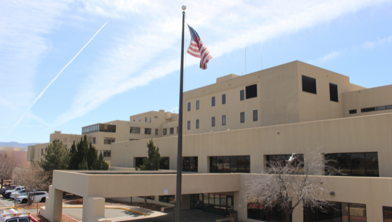 A view of the North side of the Gibson Health Hub, a five-story building with a flagpole next to a drop-off lane.