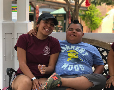 Inclusion Rec Section Block Tile Staff and child sitting on bench smiling at the audience on a warm day.