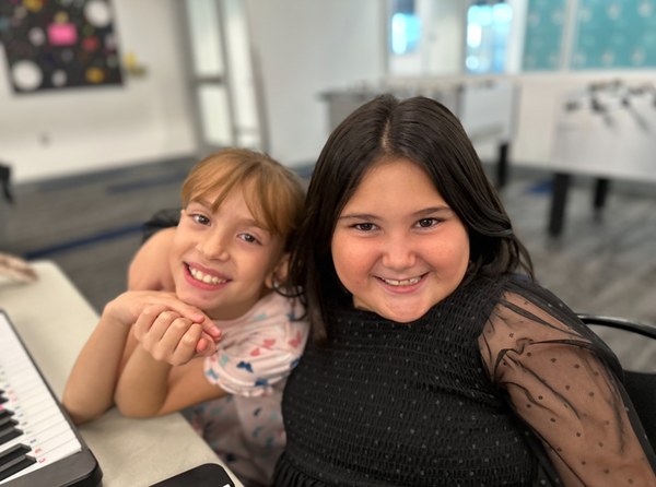 Two children smiling and hugging in a game room of a community center.