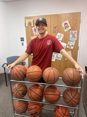 Staff in red shirt standing behind rack of basketballs