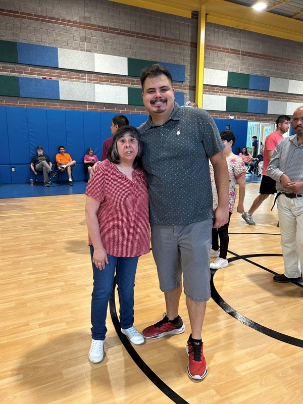 Two people pose in a gym with a crowd behind them.