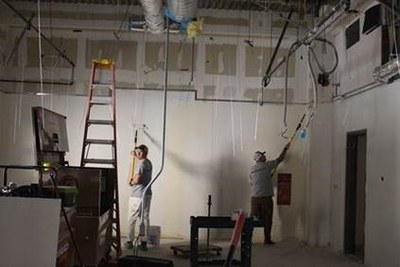 Two Painters starting to paint bare walls in a room with nothing but painting materials.