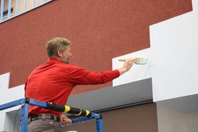Mayor Keller wearing a red shirt, using a paintbrush to add white paint to a wall.