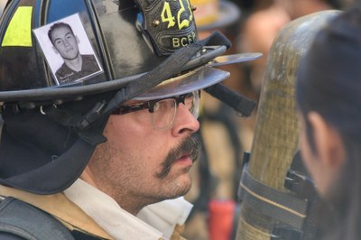 2026 911 Memorial Stair Climb BCFR Firefighter A male BCFR firefighter wearing full gear with a photo of a fallen firefighter on his helmet.