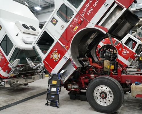 Three fire engines with their cabs tipped forward in a maintenance bay.