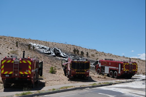F-35 crash response 2024 A group of firefighters, and 3 fire vehicles around a crash site on the side of a hill.