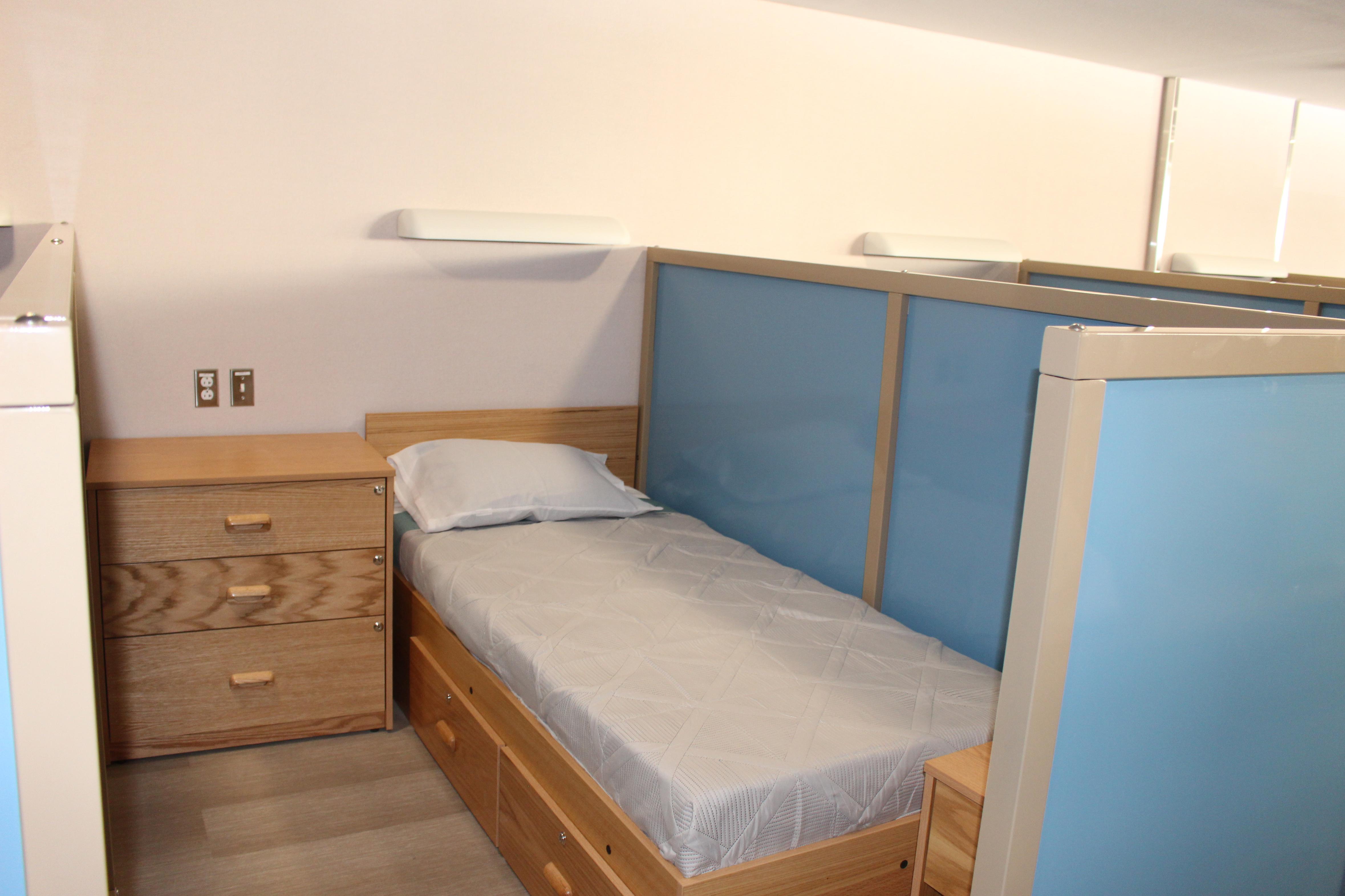 A bed in a cubicle with a blue privacy wall separating it from the next bed