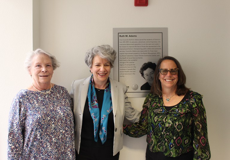 Ruth Adams's daughters Mary and Liz with stand with Ruth's friend Barbara in front of Ruth's commemorative plaque in the hallway of the health and social service center.