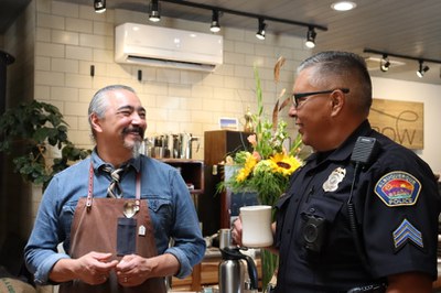 A police officer in uniform drinking coffee with a coffee shop worker.