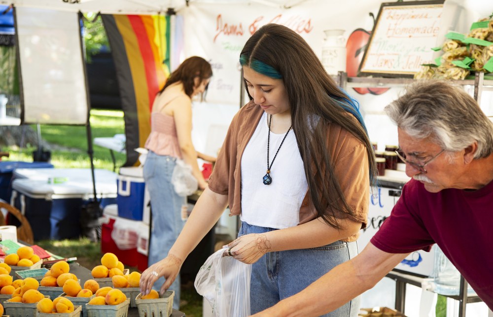 Two people choosing oranges at an outdoor market.