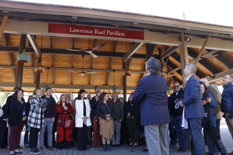 Lawrence Rael and Mayor Keller standing in front of a crowd on the Elephant Pavilion looking at a posted sign naming it "Lawrence Rael Pavilion."