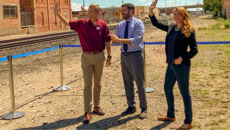 Mayor Keller, a woman, and a man waving at the Rail Yards.