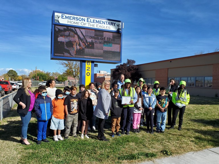 A group of students, teachers, and crossing guards pose in a line for a photo under their school's digital sign.
