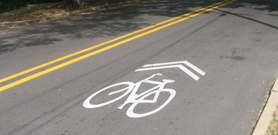 Shows a white shared lane markings or a sharrow on black asphalt.