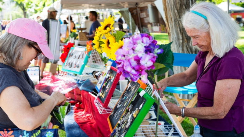 A woman buying jewelry from a vendor at a table in a park.