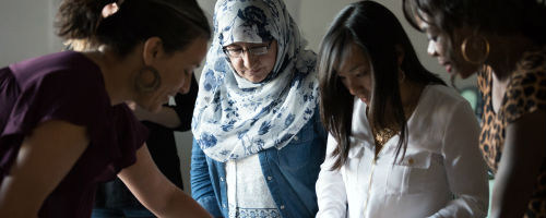 Four women looking down at something out of frame.