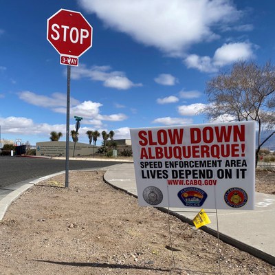 A two-sided, bilingual sign with the City of Albuquerque, Albuquerque Police, and Office of Neighborhood Coordination logos and the text "Slow Down Albuquerque! Speed enforcement area. Lives depend on it. www.cabq.gov."