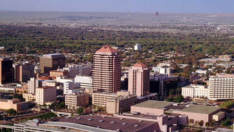 An aerial view of the downtown Albuquerque skyline with the Bosque and Rio Grande in the background.