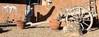 Fairwest Wagon, and old wooden wagon on a dirt road in front of a brown adobe wall with terracotta planters nearby.
