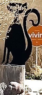 A stylized, cut-out style black metal cat sculpture mounted on a tree stump.