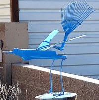 A blue roadrunner metal artwork sculpture made out of household bits and pieces like the end of a rake for the tail.