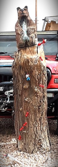 A wood sculpture, carved from a tree trunk, with a bear figure at the top.