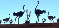 A metal artwork sculpture of four ostriches, two facing the other two in a semi-symmetrical layout, with plants in between each.