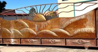 A large, copper metal gate with the embossed motif of rolling hills and a sun rising behind them.