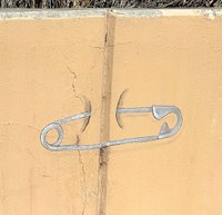 A painting of a gray safety pin between a joint in a concrete wall.