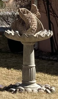 A cement water fountain with a birdbath-style base and a fish jumping out of the top.