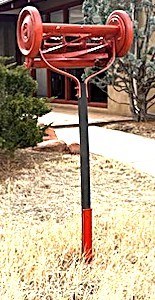 A red push lawn mower upside down with the handle stuck into the ground.