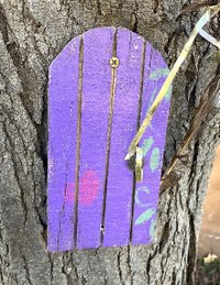 A purple painted fairy door mounted to the side of a tree.