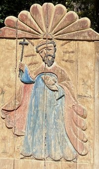 A relief wood carving of a saint holding up a cross.