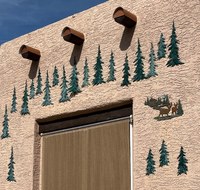 Evergreen trees painted onto an adobe wall surrounding a door.