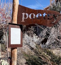 A metal flag attached to a wooden poll. The word "poetry" is punched out of the metal.