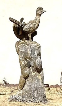 A wood carving sculpture of a roadrunner on top of a tree stump.