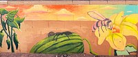 A painted wall art mural with a watermelon, a yellow flower, and an ant on the watermelon.