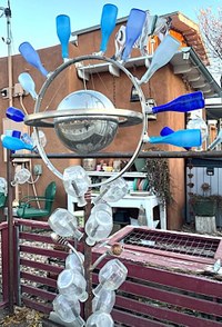 A metal sculpture with a Saturn-like planet in the center and a single ring surrounding it with blue glass bottles attached.