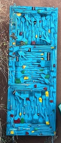 A modern artwork sculpture of a door covered in paintbrushes painted turquoise.