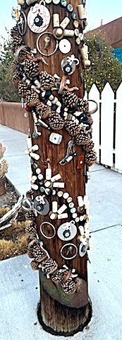 A telephone poll covered in artfully arranged objects, like an upward spiral made out of pinecones, as well as bottle caps and other knickknacks.