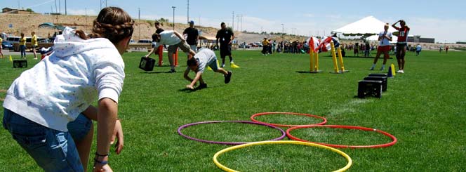 Kids participating in various field day events with adults cheering them on.