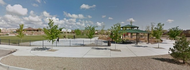 A park with a basketball court, covered picnic table area, and grass field with trees.