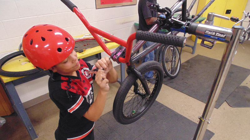 A young child wearing a red bike helmet working on a bike.