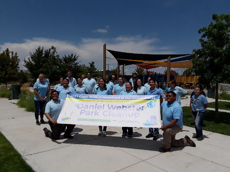 Group photo of Daniel Webster Cleanup volunteers outdoors next to a park. The volunteers are wearing sky blue colored polo shirts and are holding up a banner that reads: 2021 Clean World Movement in the United States. Daniel Webster Park Cleanup in bold.